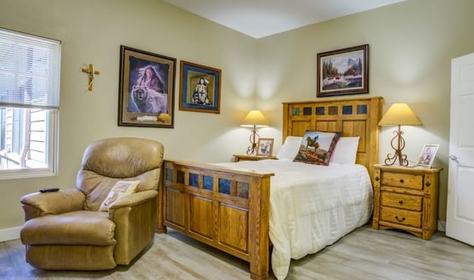 A well-furnished bedroom with a bed, armchair, and artwork.