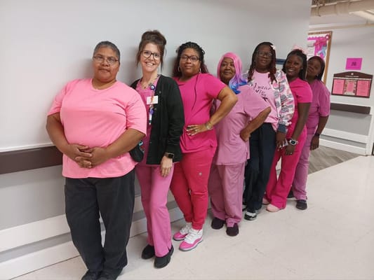 Group of staff members wearing pink clothing in a hallway.