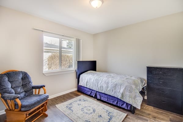 A well-lit bedroom with a single bed, chair, and dresser.