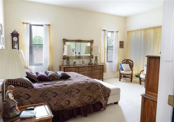 A well-lit bedroom with a bed, dresser, and seating area.
