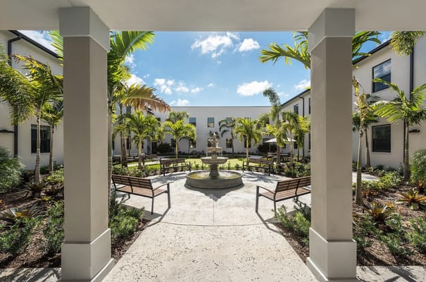 A serene courtyard with a fountain surrounded by palm trees and benches.