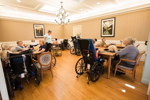 Residents participating in activities in a bright common room with wheelchairs