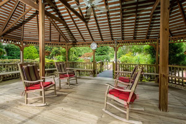 Seating area in a gazebo with rocking chairs and lush greenery
