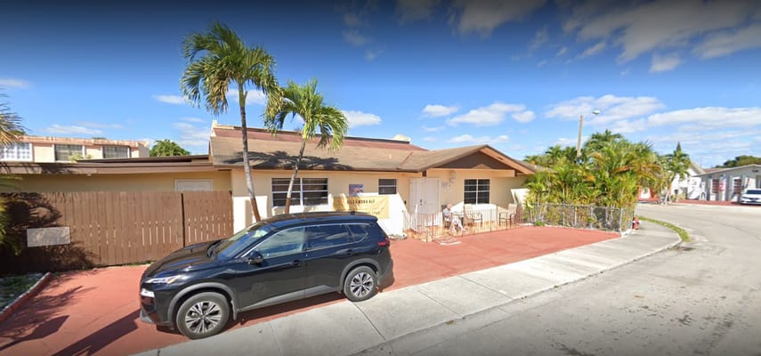 Front exterior of Villa Nora ALF Inc. with palm trees and a parked car.