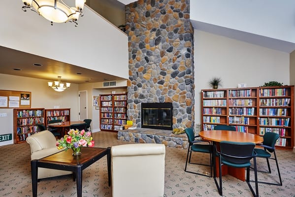Lounge area with a stone fireplace, bookshelves, and seating in Westmont of Chico