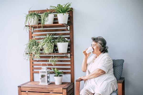 Senior woman sipping tea while seated next to indoor plants.