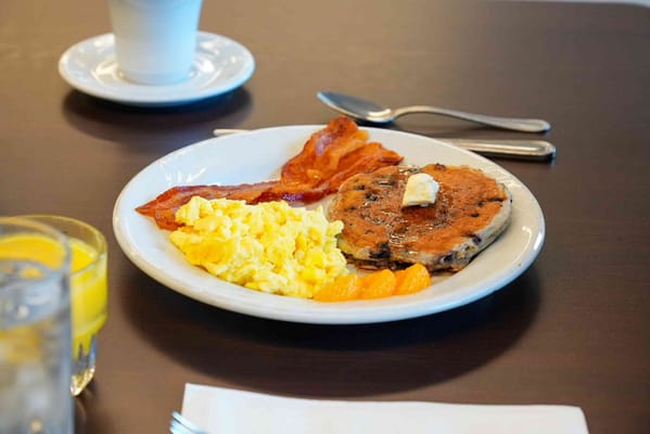 A hearty breakfast plate with eggs, bacon, pancakes, and fruit