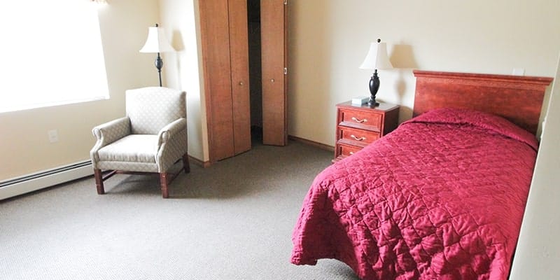 A bedroom with a bed, a chair, and a lamp.