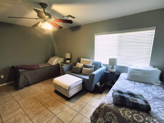 A cozy bedroom with two beds, a sofa, and natural light from a window.