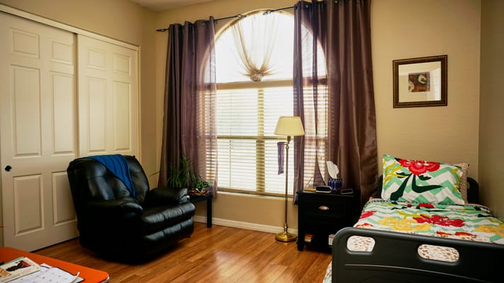 A cozy bedroom with a bed, a black chair, and a window with natural light.