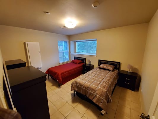 A spacious bedroom with two beds and bedside tables, featuring a window with natural light.