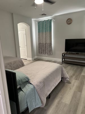 A well-lit bedroom featuring two beds, a TV, and decorative curtains.