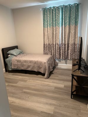 A cozy bedroom with a bed, a patterned curtain, and a TV stand.