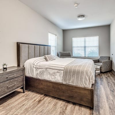 A well-furnished bedroom in Iris Memory Care with a bed and a chair.