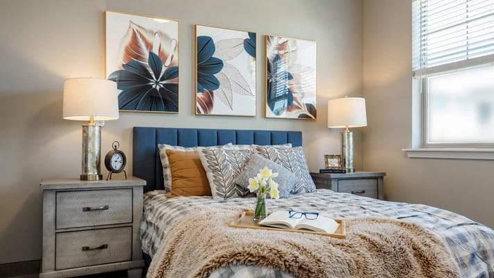 Bright, cozy bedroom with floral artwork and bedside lamps