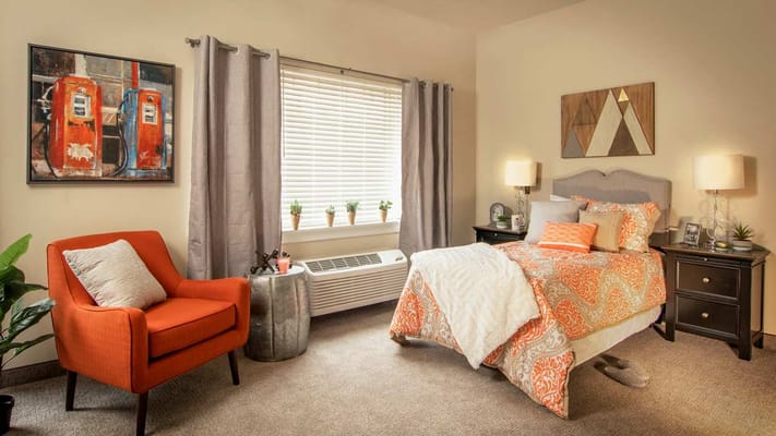 A beautifully decorated bedroom with an orange chair and colorful bedding.