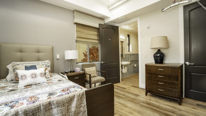 Comfortable senior bedroom featuring a bed, chair, and access to a bathroom