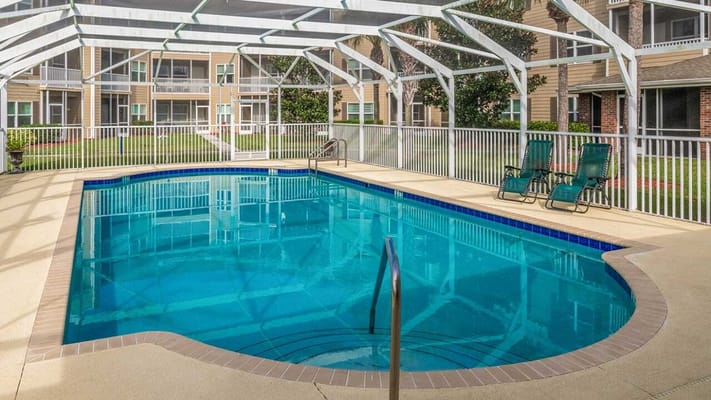Clear blue swimming pool with lounge chairs under a screened enclosure