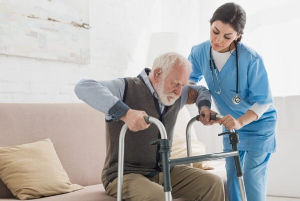 Caregiver assisting an elderly man with a walker in a cozy room