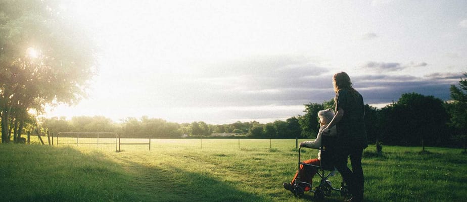 Caregiver pushing a resident in a wheelchair through a grassy area