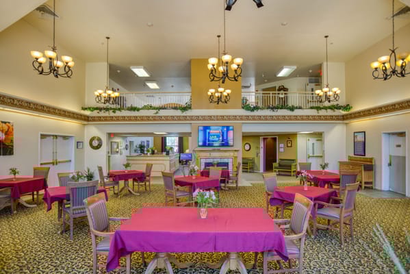 Spacious dining room with tables set for meals, featuring chandeliers and a welcoming atmosphere.