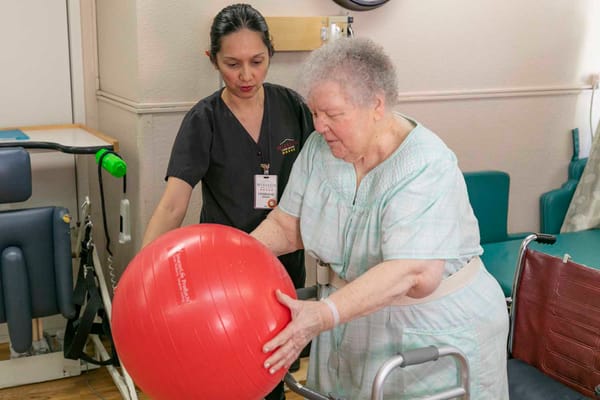 Staff assisting a resident with a therapy ball in a room