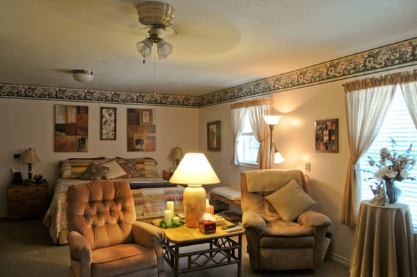 A well-furnished bedroom featuring a bed, two chairs, and decorative art on the walls.