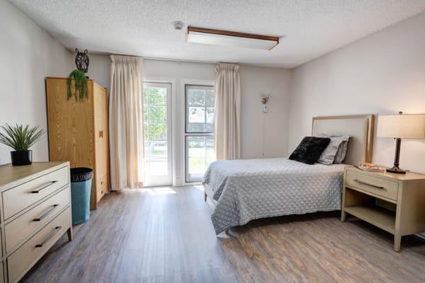 A well-lit bedroom with a bed, dresser, and curtains.