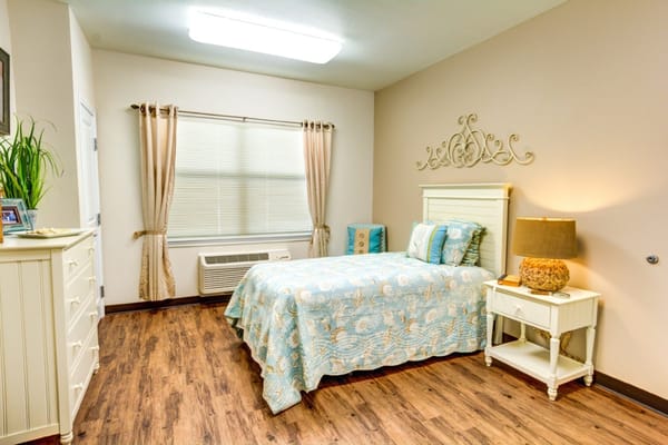 Bedroom featuring a bed with a light blue quilt, wooden furniture, and natural light from a window.