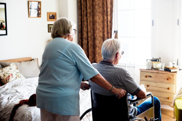 An elderly woman assisting a man in a wheelchair in a cozy room