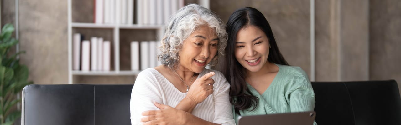 A senior woman and a younger woman smiling at a tablet together