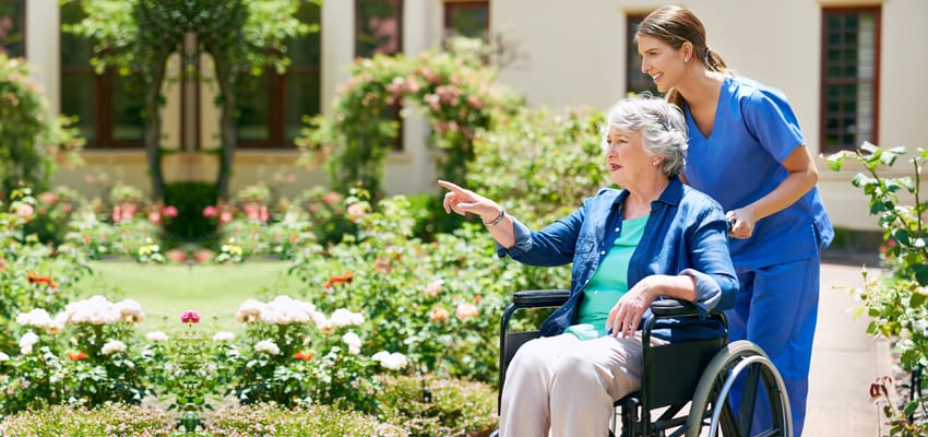 A caregiver pushing a resident in a wheelchair through a garden