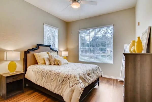 A cozy bedroom featuring a queen-sized bed, nightstands, and large windows.