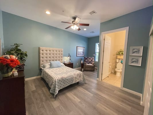 A beautifully decorated bedroom with a bed, chair, and bathroom entrance.