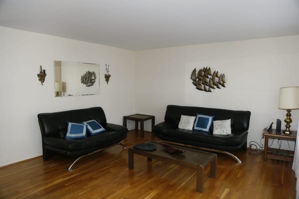 A living room with black leather sofas and wooden flooring