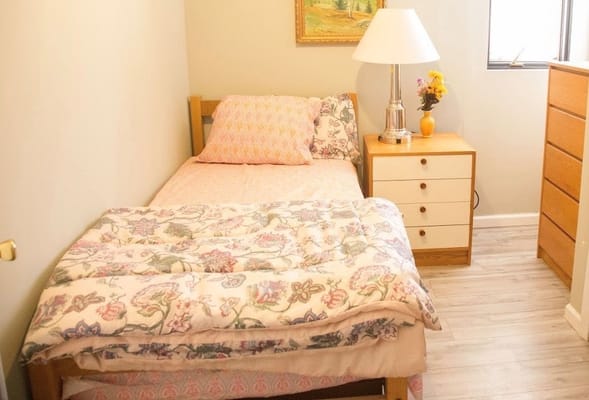 A cozy bedroom with a single bed, nightstand, and lamp.