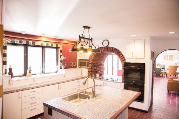 Spacious kitchen with tile countertops and a brick archway.