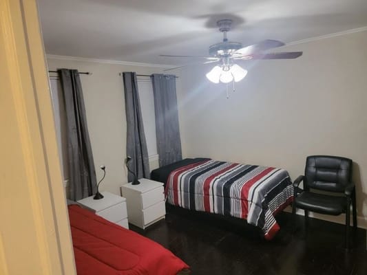 A cozy bedroom with two beds, a chair, and a ceiling fan