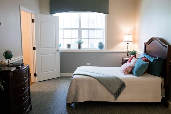 A well-decorated bedroom with a bed, pillows, and a lamp by the window.