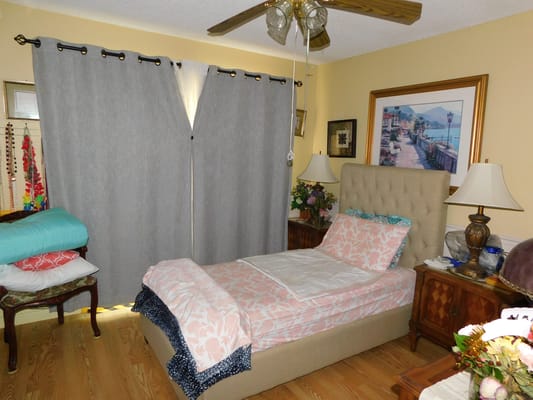 A well-decorated bedroom with a bed, side tables, and a large window with gray curtains.