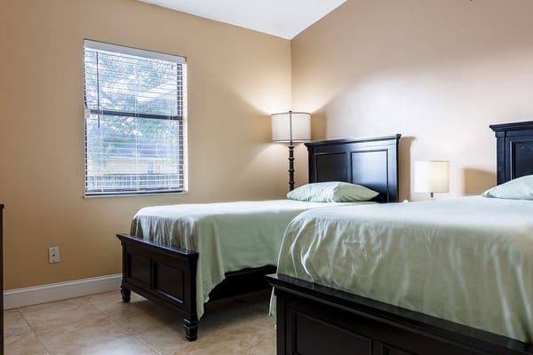 Two beds with light green bedding in a well-lit bedroom