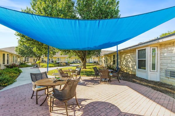 Outdoor seating area with tables and chairs under a blue shade sail.