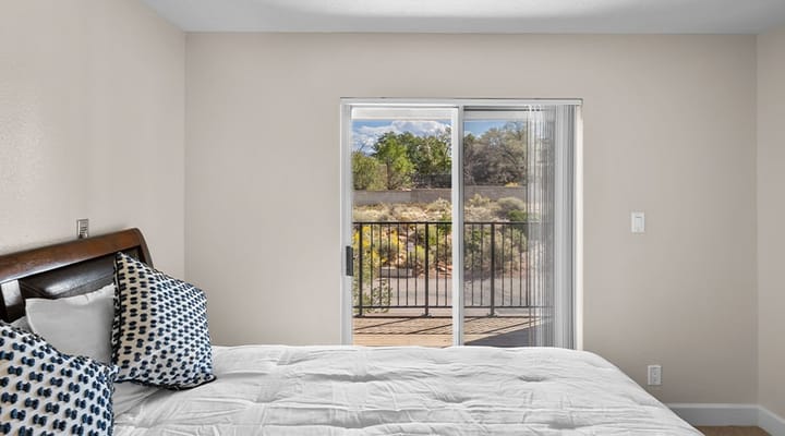 Bright bedroom featuring a bed with decorative pillows and a sliding glass door to a balcony.