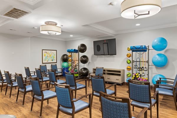 A well-equipped exercise room with chairs, fitness equipment, and a television.