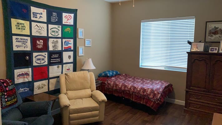 A cozy bedroom with a quilted wall hanging, a bed, and an armchair.