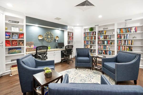 Comfortable seating area in library with bookshelves and a desk.