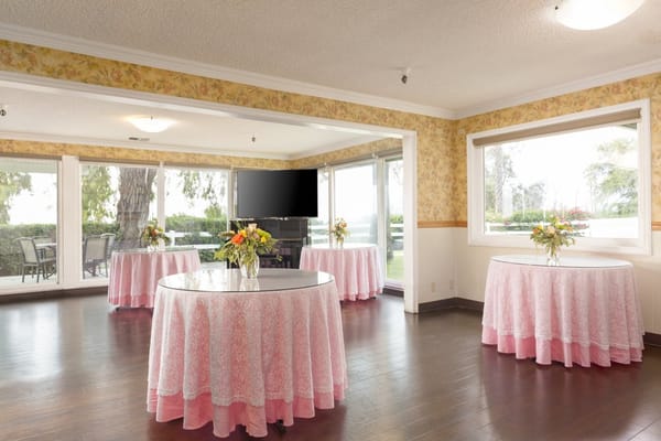 Bright event space with round tables, floral decorations, and large windows.