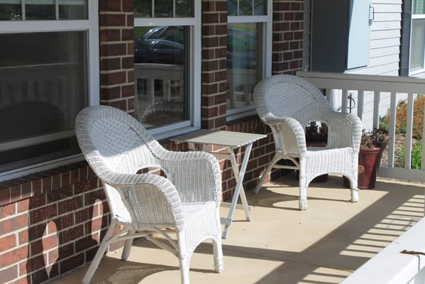 Two white wicker chairs and a small table on a porch