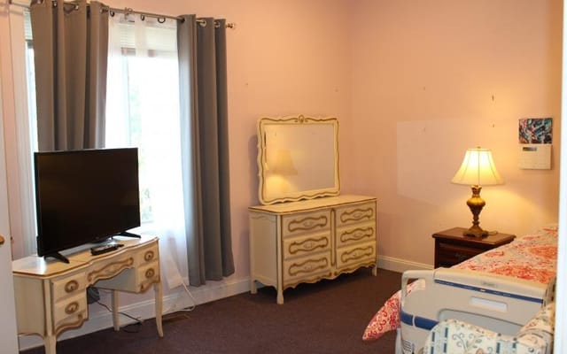 A bright living space featuring a TV, dresser, and bedside lamp.