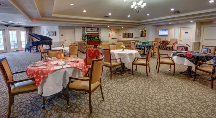 Interior of a living room with tables and chairs, featuring a piano in the background.